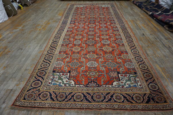 Orange runner rug with an all-over multicolor floral pattern and wide navy borders on distressed wood.