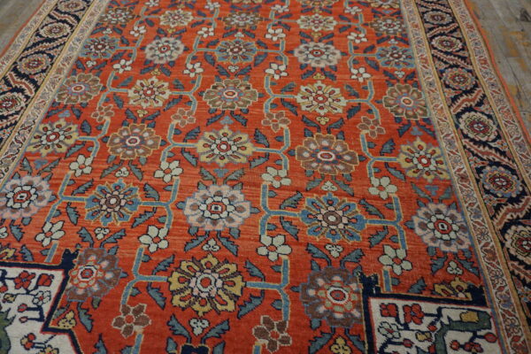 Orange rug with detailed blue and cream floral lattice pattern and a navy border on a wood floor.
