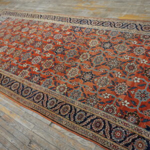 Oversized burnt orange rug with dense floral patterns, wide navy borders, displayed on distressed wooden floor planks.