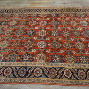 Rust-colored rug with ornate blue, gold, and cream floral patterns and a dark navy border on wood planks.