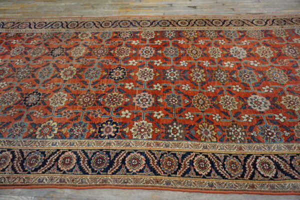 Rust-colored rug with ornate blue, gold, and cream floral patterns and a dark navy border on wood planks.