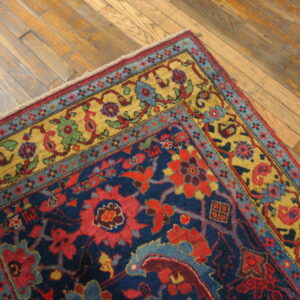 A deep navy blue rug with red and gold traditional patterns rests on distressed wood flooring.