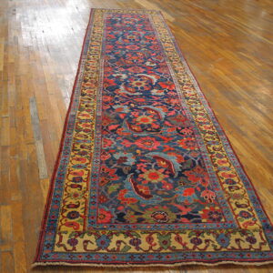 Blue and red patterned runner rug with gold borders displayed on light brown hardwood planks.