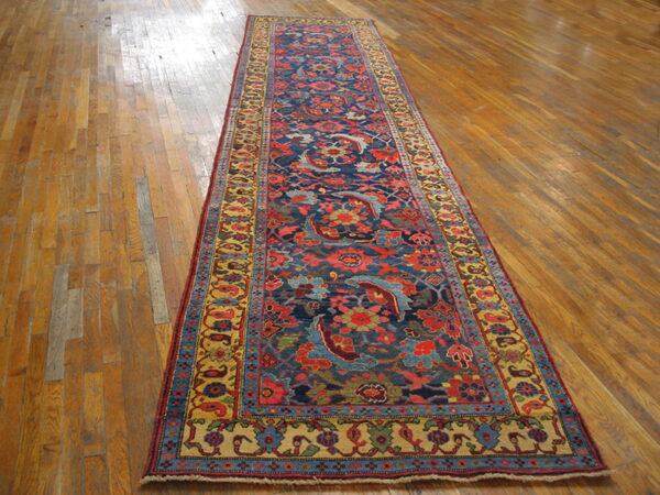 Blue and red patterned runner rug with gold borders displayed on light brown hardwood planks.