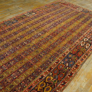 Ornate striped rug with red, gold, and dark blue patterns rests on distressed plank flooring.