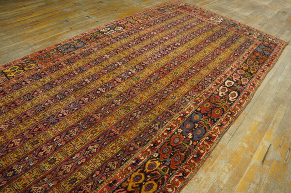 Ornate striped rug with red, gold, and dark blue patterns rests on distressed plank flooring.