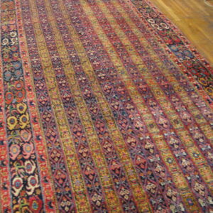 Ornate traditional runner rug with vertical stripes of red, blue, and yellow patterns on wood flooring.
