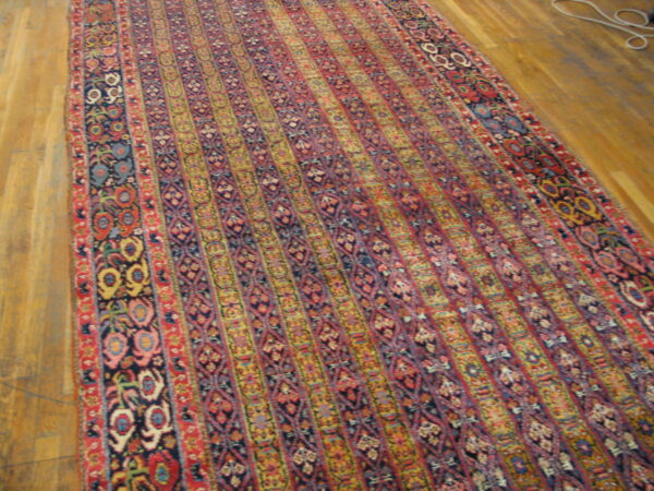Ornate traditional runner rug with vertical stripes of red, blue, and yellow patterns on wood flooring.