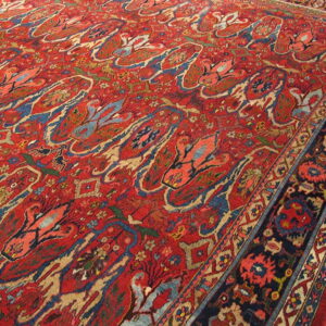 Red pile rug with blue and tan abstract floral motifs and a complex dark border on wood floor.