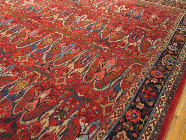 Red pile rug with blue and tan abstract floral motifs and a complex dark border on wood floor.