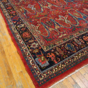 Red patterned area rug with a detailed navy border displayed on golden hardwood planks.