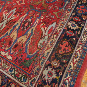 Red rug featuring stylized floral patterns and a navy border, lying on light wood planks.