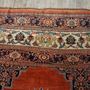 The border of a traditional rust, navy, and cream rug with floral patterns rests on weathered wood planks.