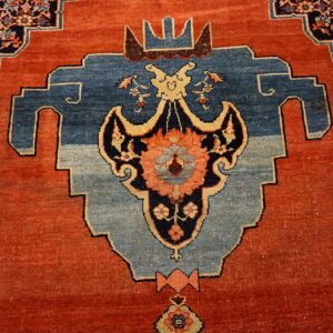 Intricate rug pattern featuring a rust-red field and a large stepped blue medallion with cream outlines.