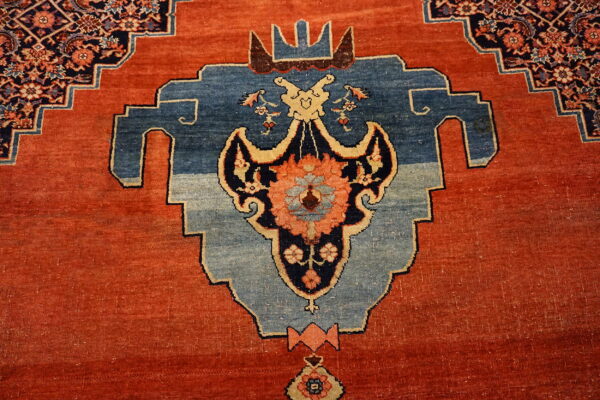 Intricate rug pattern featuring a rust-red field and a large stepped blue medallion with cream outlines.