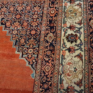 Close-up of a rug featuring an orange field, a stepped blue design, and detailed cream and navy floral borders.