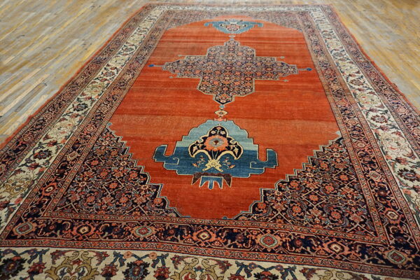 Traditional orange rug with detailed navy and blue patterns, placed on light, worn hardwood flooring.