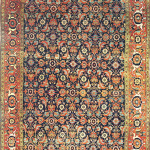 A colorful rug with a deep navy field, dense floral pattern in orange and teal, and a wide primary red border.