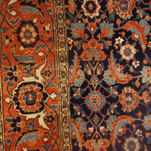 Detail of a traditional floral rug with navy and rust coloring resting on light wood planks.