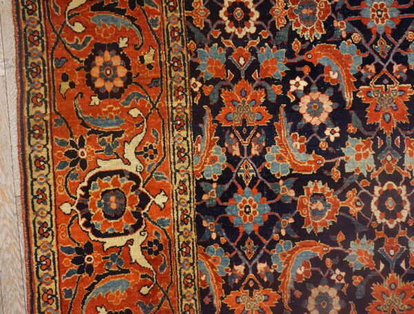 Detail of a traditional floral rug with navy and rust coloring resting on light wood planks.