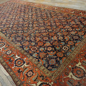 Large traditional rug featuring a dense navy, rust, and blue pattern on gray wooden flooring.