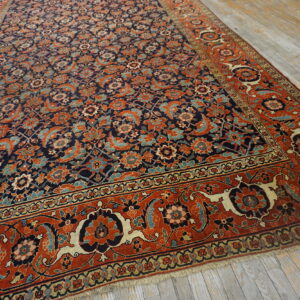 Angled view of a navy and rust floral rug with an intricate pattern on distressed gray wood floors.