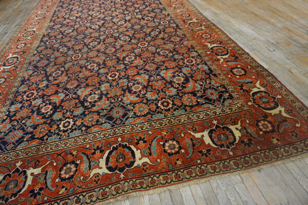 Angled view of a navy and rust floral rug with an intricate pattern on distressed gray wood floors.