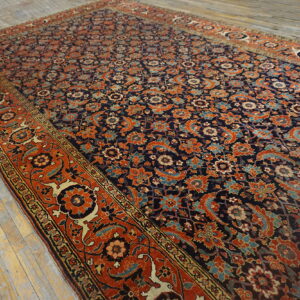 A densely patterned rug with a dark field and rust border rests on pale, weathered wood planks.