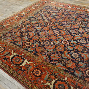 Ornate navy and rust-colored rug with complex floral patterns placed diagonally on gray wood floors.