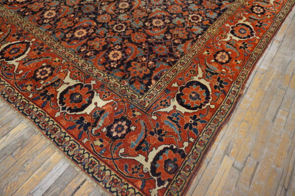 Ornate floral rug featuring dark blue and rust tones on distressed light wooden flooring.