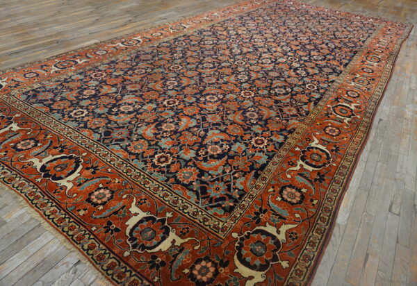 A large navy and terracotta rug with a detailed floral pattern lies on gray hardwood floors.