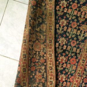 A deep indigo floral rug with red and tan motifs is partially rolled on white tile.