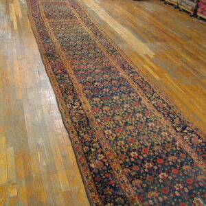Long runner rug featuring a dense navy and red floral pattern on light wooden floorboards.