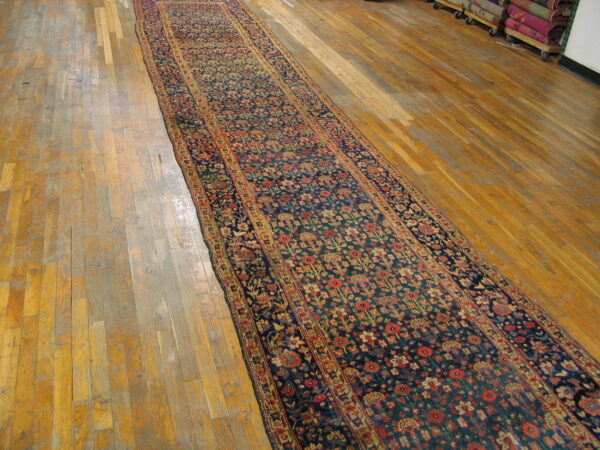 Long runner rug featuring a dense navy and red floral pattern on light wooden floorboards.