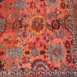 Traditional rug detail with a vibrant coral field and stylized medallion patterns in slate blue, red, and gold.