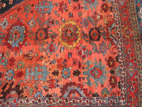Traditional rug detail with a vibrant coral field and stylized medallion patterns in slate blue, red, and gold.