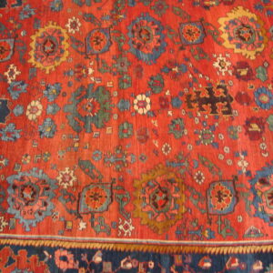 Vibrant red rug displaying dense geometric and stylized floral patterns in blue, gold, and dark green.