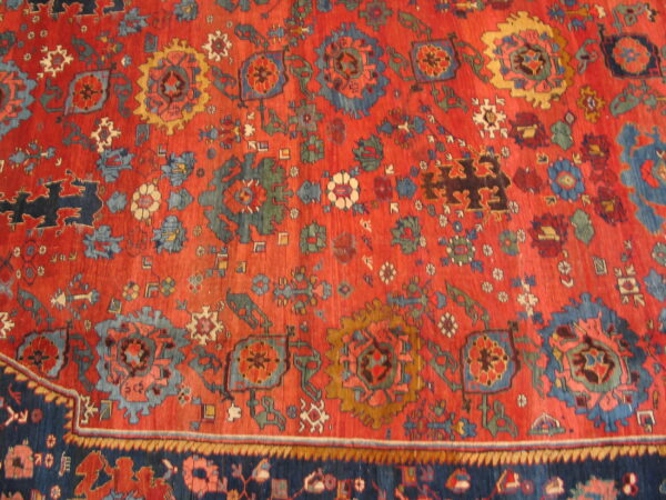 Vibrant red rug displaying dense geometric and stylized floral patterns in blue, gold, and dark green.