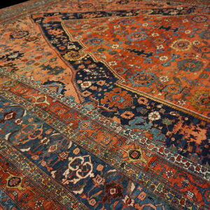 Low-pile rug detail in terracotta and navy blue with detailed floral and geometric borders.