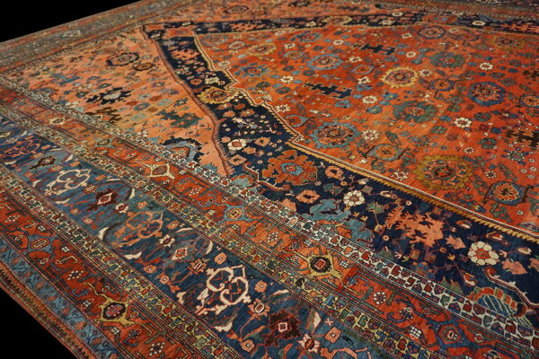 Low-pile rug detail in terracotta and navy blue with detailed floral and geometric borders.