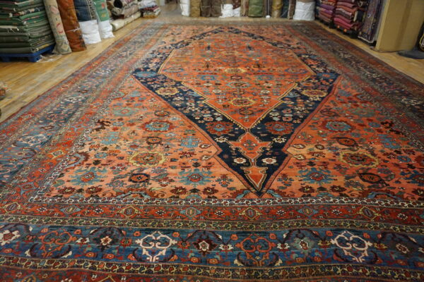 Vibrant orange and blue patterned area rug lying flat on wood flooring, surrounded by stacks of rolled rugs.