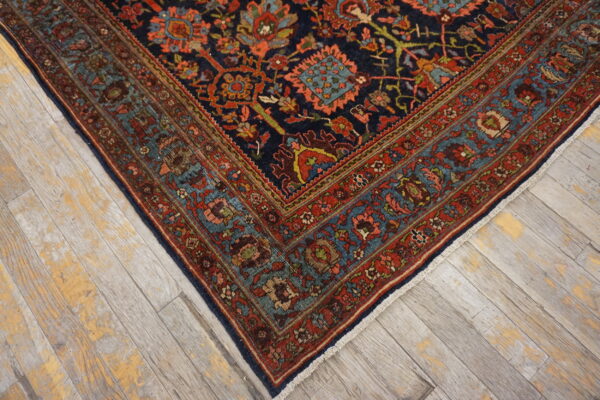 Corner view of a dark blue rug with elaborate red and teal borders on weathered wood floors.