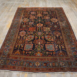 Navy and rust patterned area rug with complex floral designs sits on distressed whitewashed wood floor.