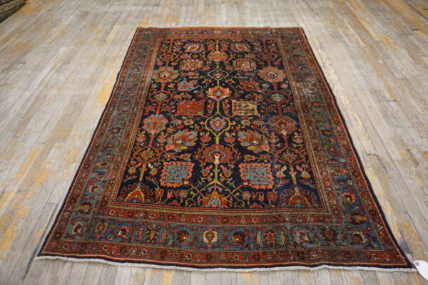 Navy and rust patterned area rug with complex floral designs sits on distressed whitewashed wood floor.