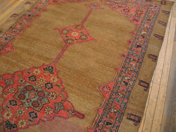 Traditional rug with a muted camel field, red geometric medallions, and detailed borders on wood flooring.