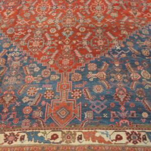 Red and blue geometric rug with stylized motifs and a contrasting cream and maroon border visible at the bottom.