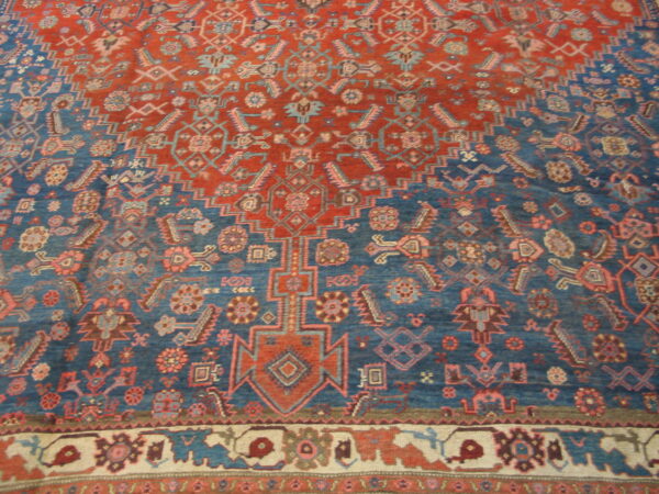 Red and blue geometric rug with stylized motifs and a contrasting cream and maroon border visible at the bottom.