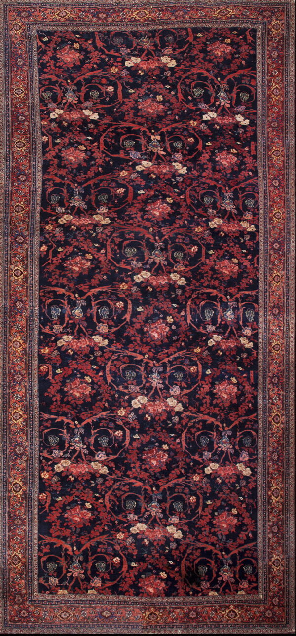Dark blue rug with a dense pattern of red florals and vines, featuring a detailed multi-colored border.