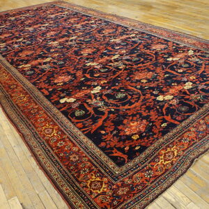 Navy and rust floral rug featuring intricate patterns and borders covers distressed wide plank wood floors.