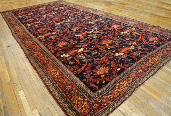 Navy and rust floral rug featuring intricate patterns and borders covers distressed wide plank wood floors.
